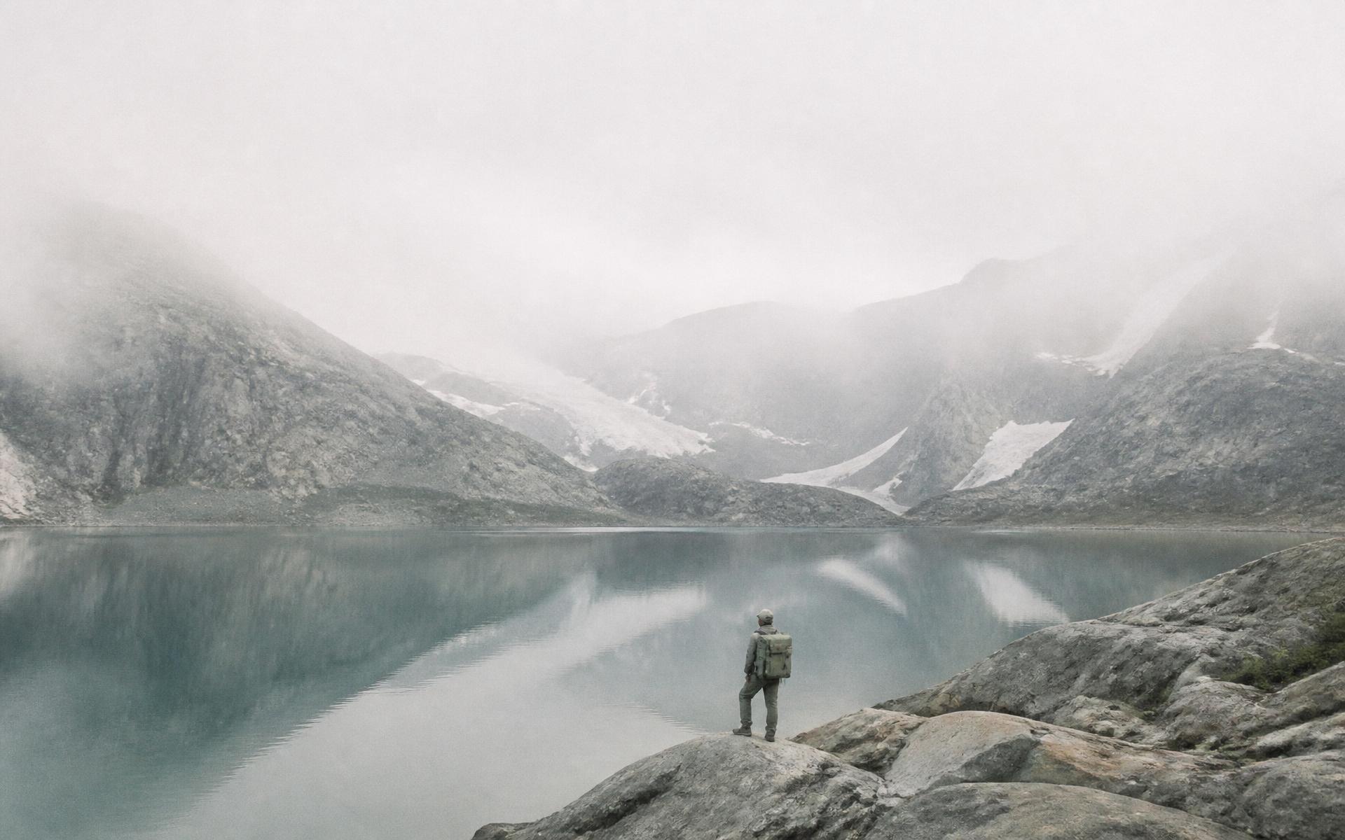 A lone traveller with a WildbearX pack on the shore of a misty alpine lake